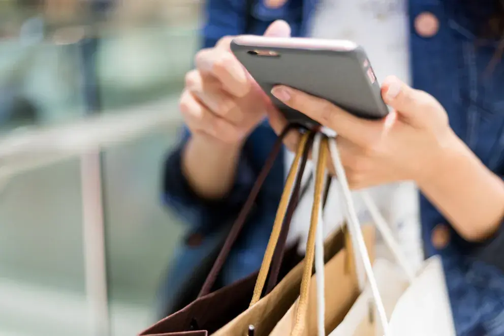 close up of person using cell phone holding shopping bags