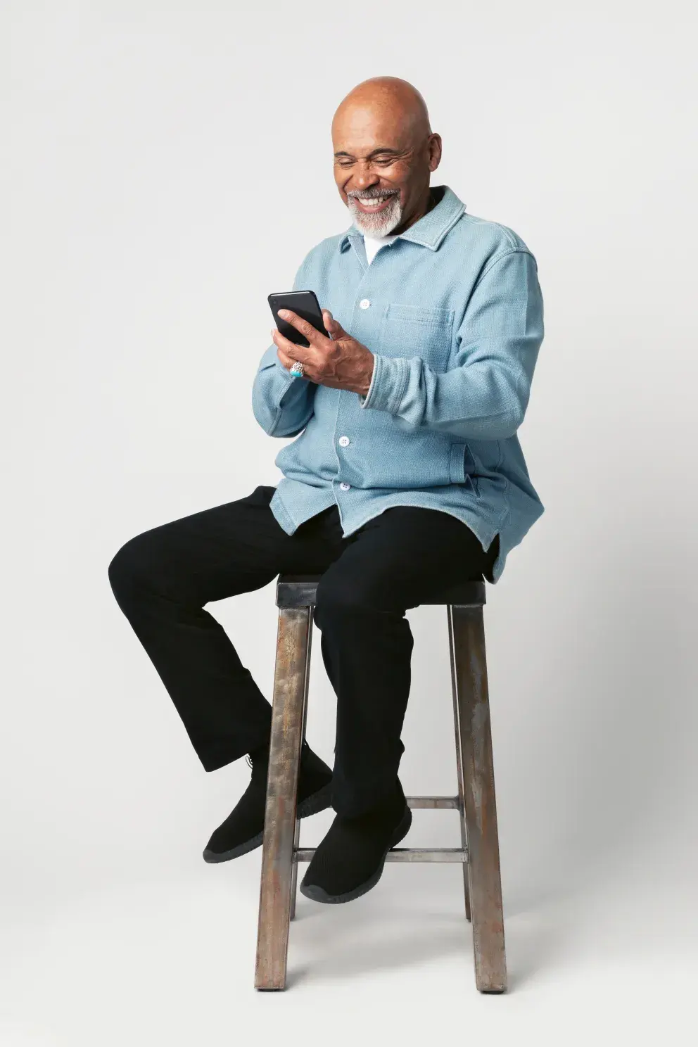 smiling senior man sitting on bar stool using cell phone