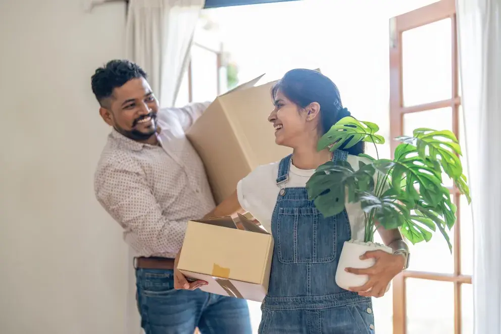 Smiling couple carrying moving boxes and a plant into their new home. Smiling couple carrying moving boxes and a plant into their new home.