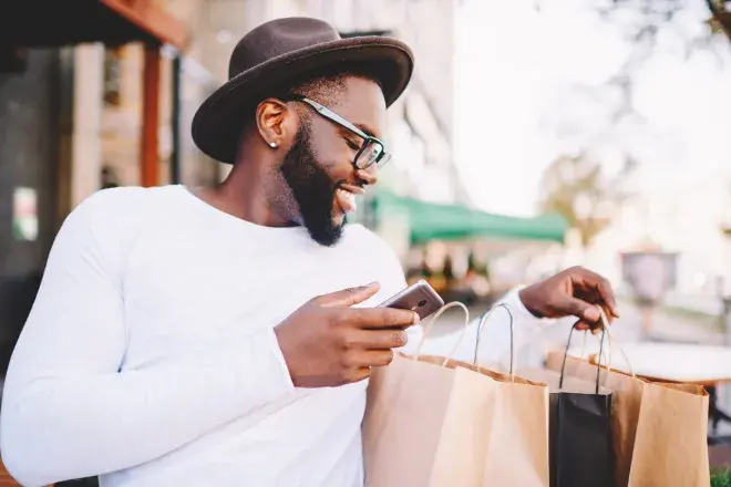smiling man looking through shopping bags and using cell phone