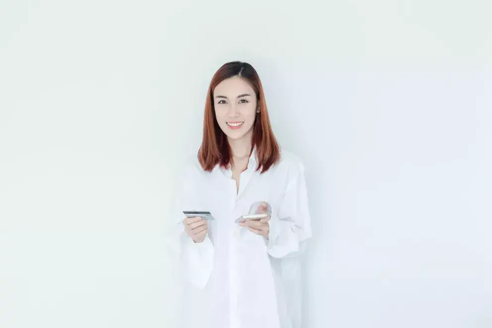 Young woman in white shirt smiling while holding a phone and notepad.