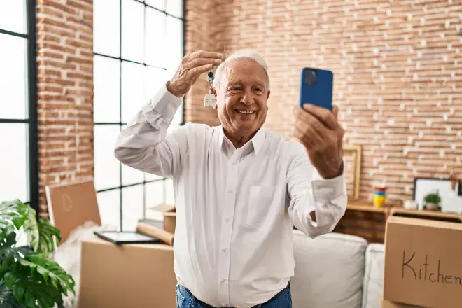 excited man holding new house keys up to phone to take selfie
