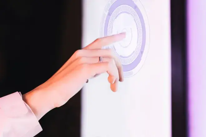 Hand reaching out to touch a glowing circular button on a white touchscreen panel against a dark background. Hand reaching out to touch a glowing circular button on a white touchscreen panel against a dark background.