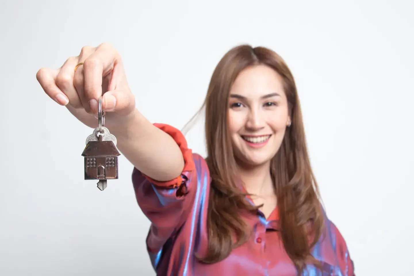 Smiling woman with long brown hair holding out house keys toward camera Smiling woman with long brown hair holding out house keys toward camera